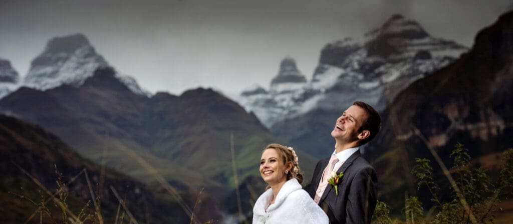 Bride and groom standing in front of snow capped mountain peaks