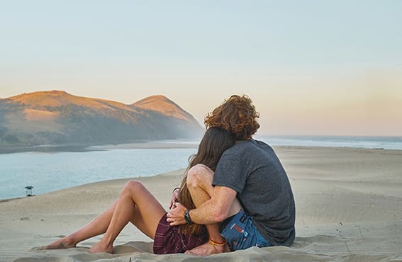 Couple sitting on the beach looking out towards the horizon