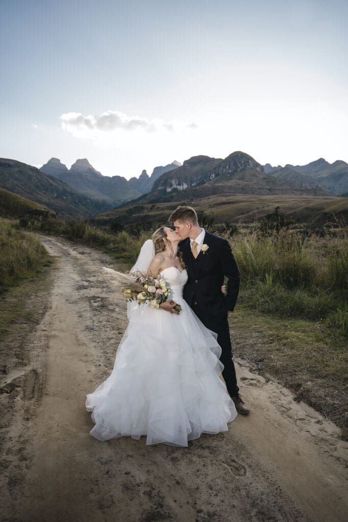 Matt&Stacey-455 Cathedral-Peak Bride and groom kissing on dirt road with mountain range behind