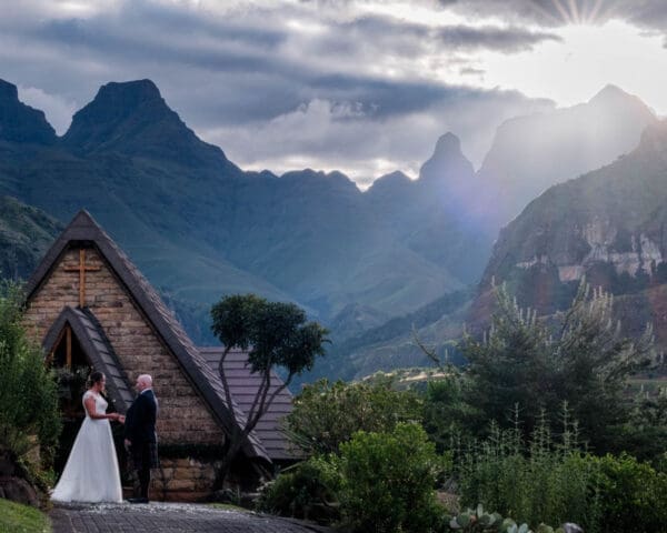 View of couple in front of chapel with sunset over the mountain peaks.