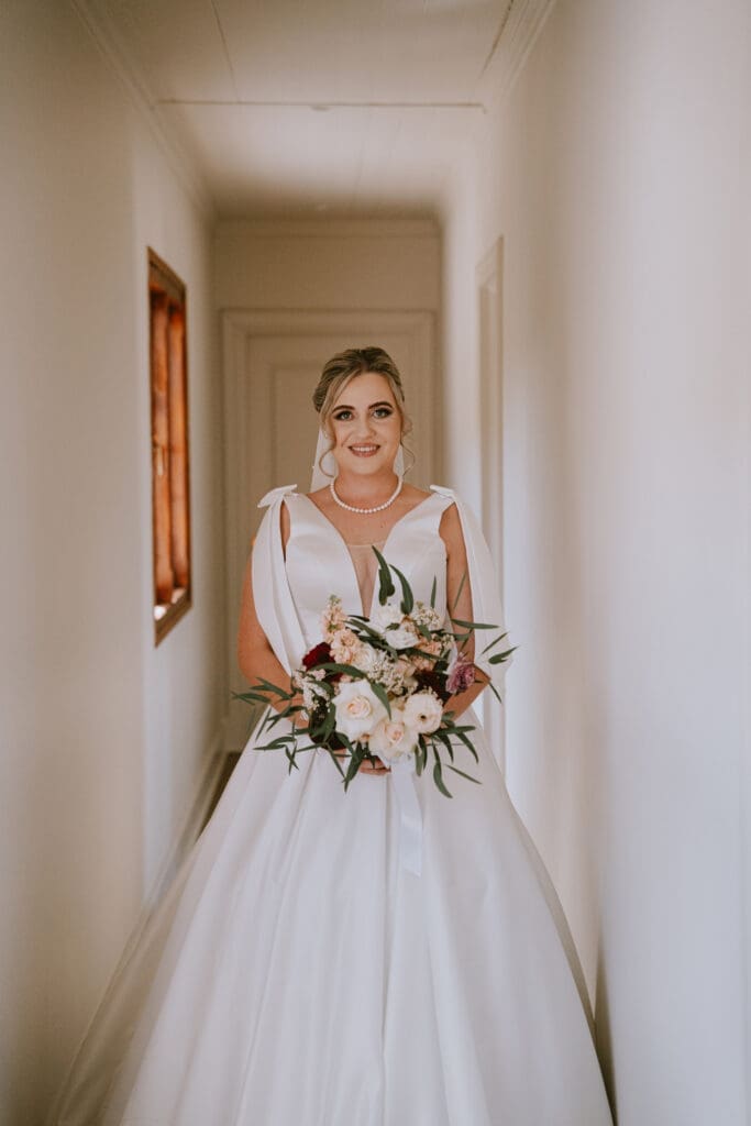 Bride standing in passage holding elegant white and neutral bouquet