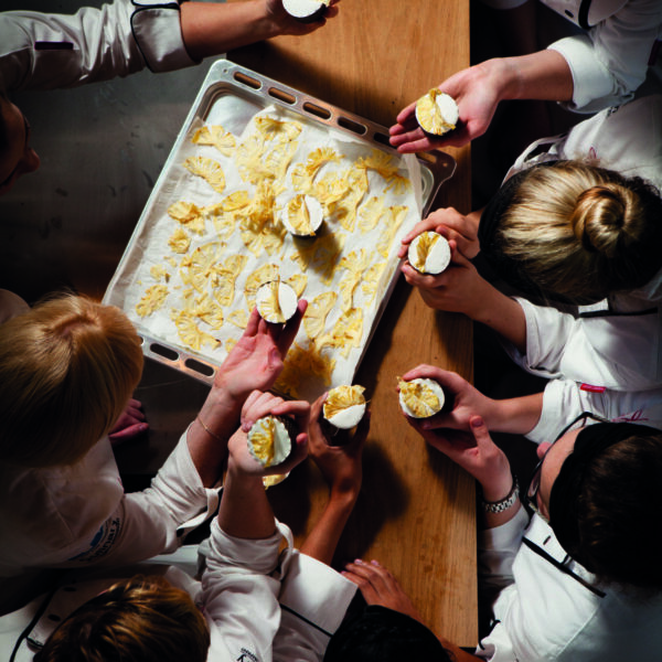 Chef Jackie Cameron and team of students hovering over tray of pastries