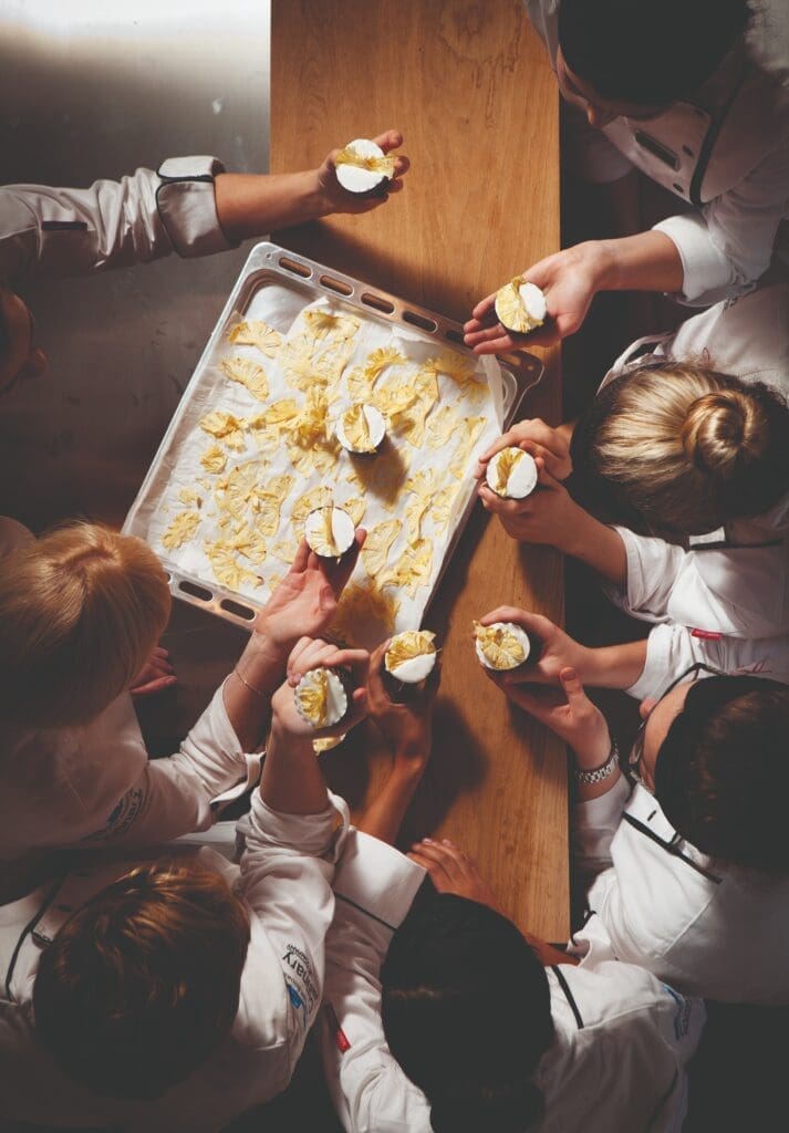 Group of chefs reaching to take pastries off baking sheet
