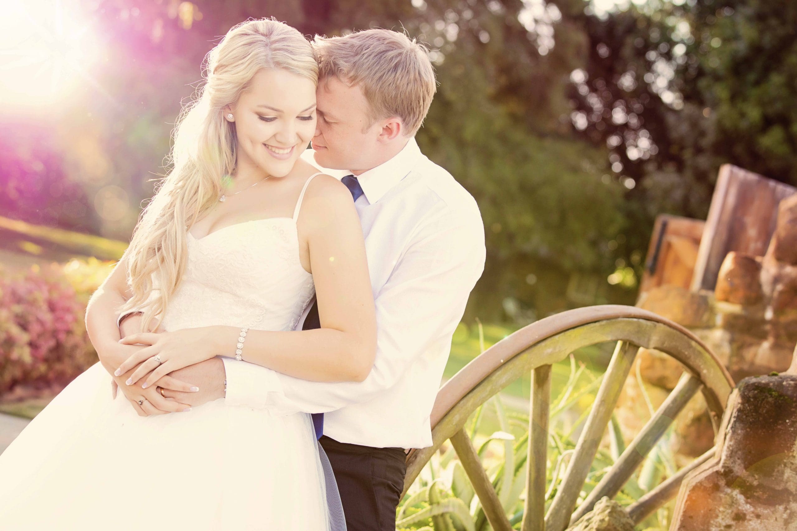 Bridal couple snuggle against wagon wheel