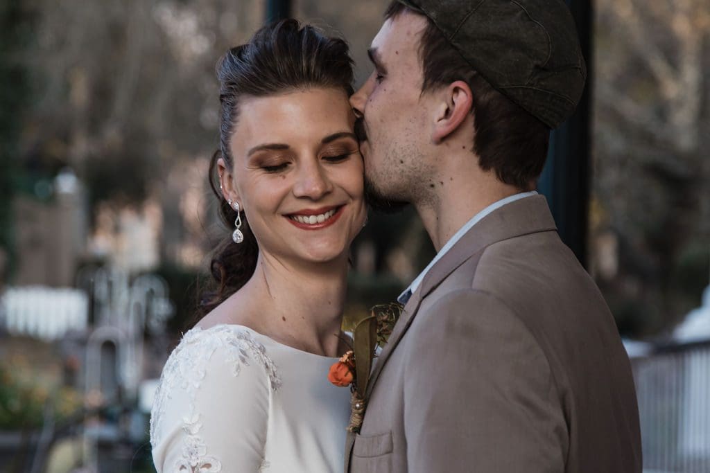 Smiling bride gets kissed on cheek by groom