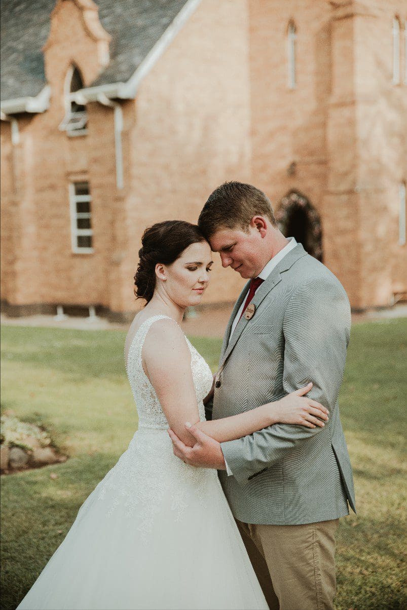 Bride and groom standing forehead to forehead in front of chapel