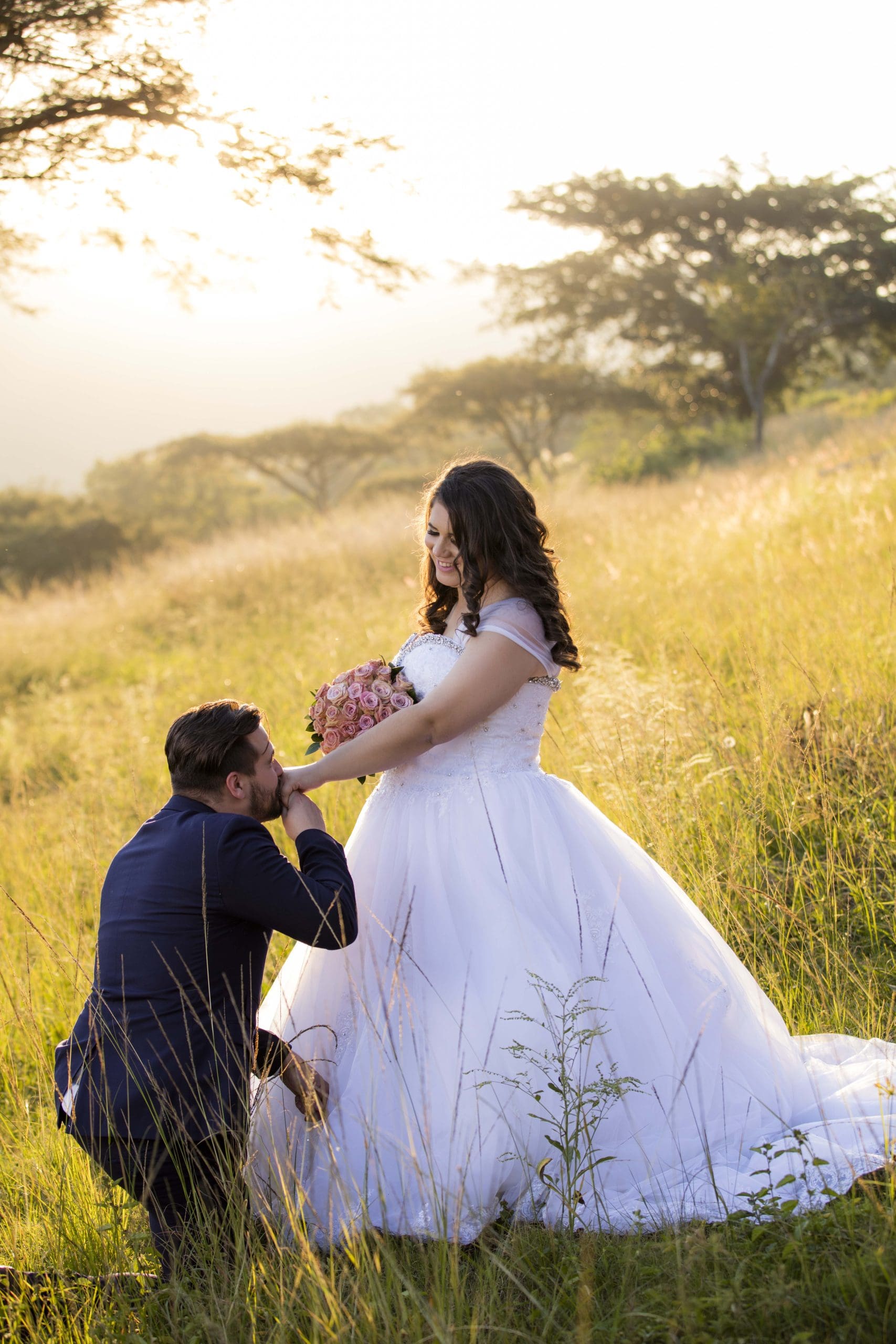 Groom on bended knee kissing bride's hand