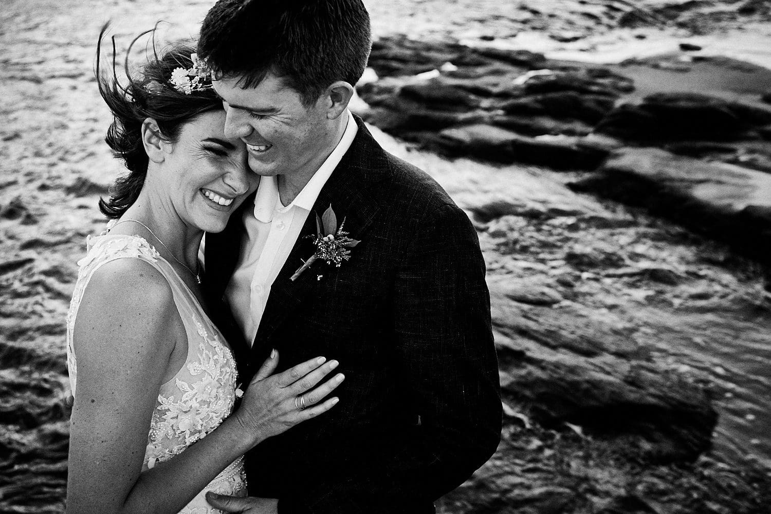 Bride resting head on groom's shoulder at beach