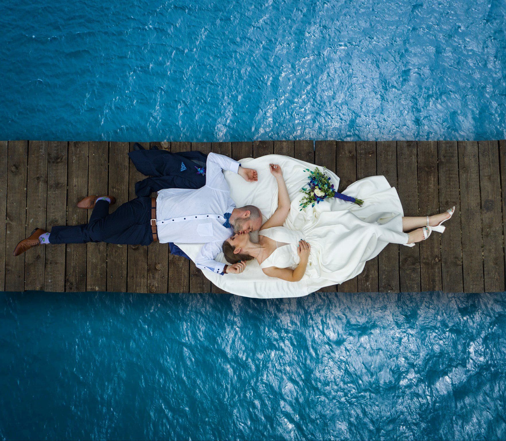 Drone shot of couple lying down on wooden jetty