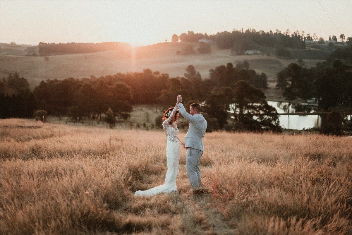 Bride and groom dancing in field at sunset
