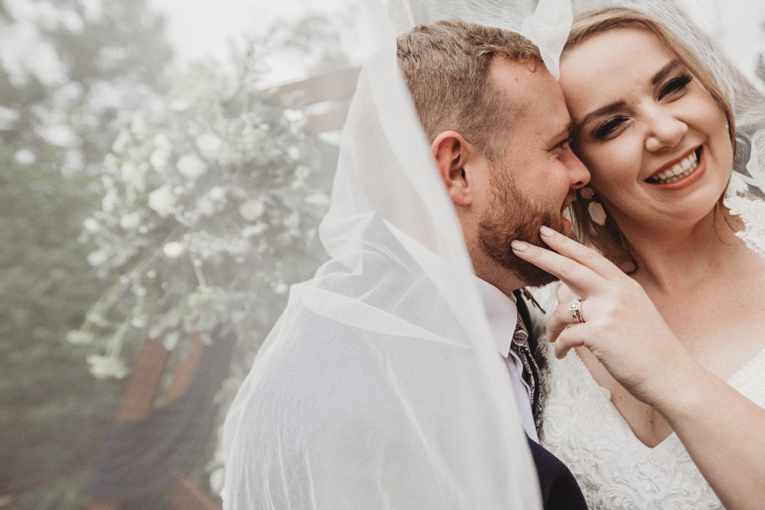 Groom whispers into brides ear wrapped in veil