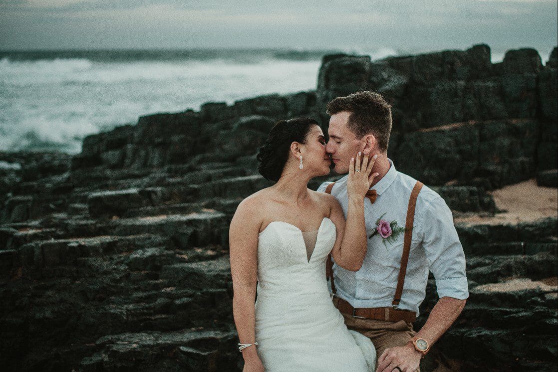 Bride kissing groom behind her on beach