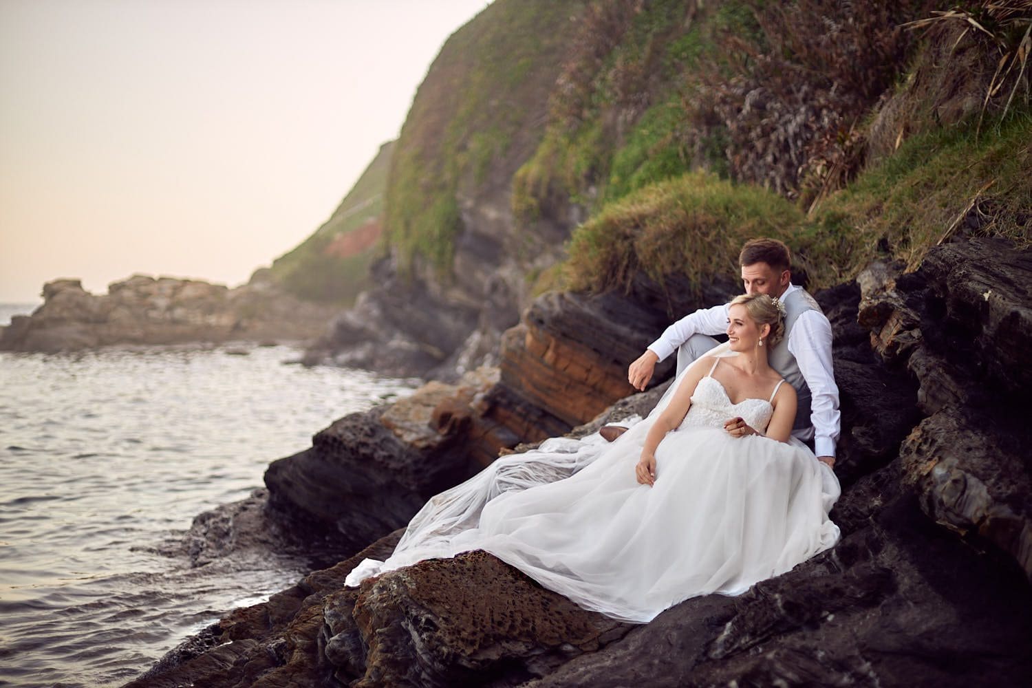 Bride and groom sitting on rocks looking at ocean