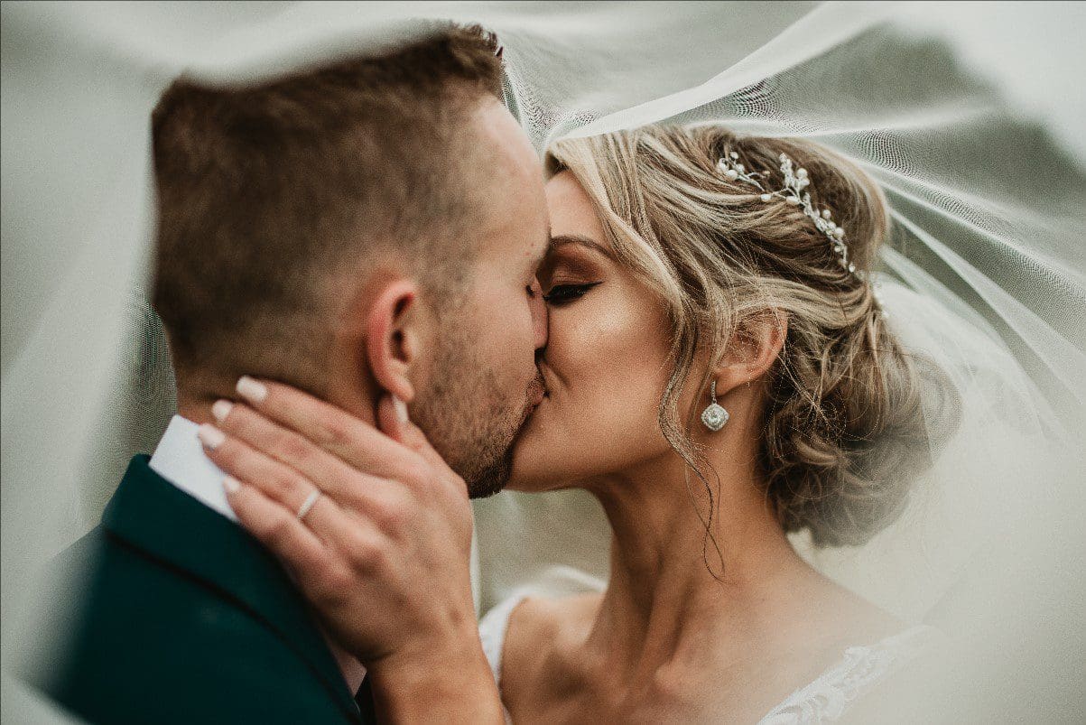 Bride and groom kissing beneath veil