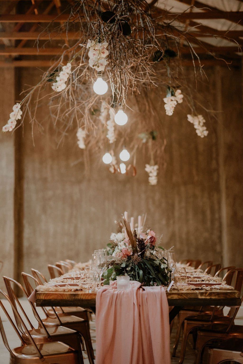 Blooms, dried branches and hanging lights above elegant table setting