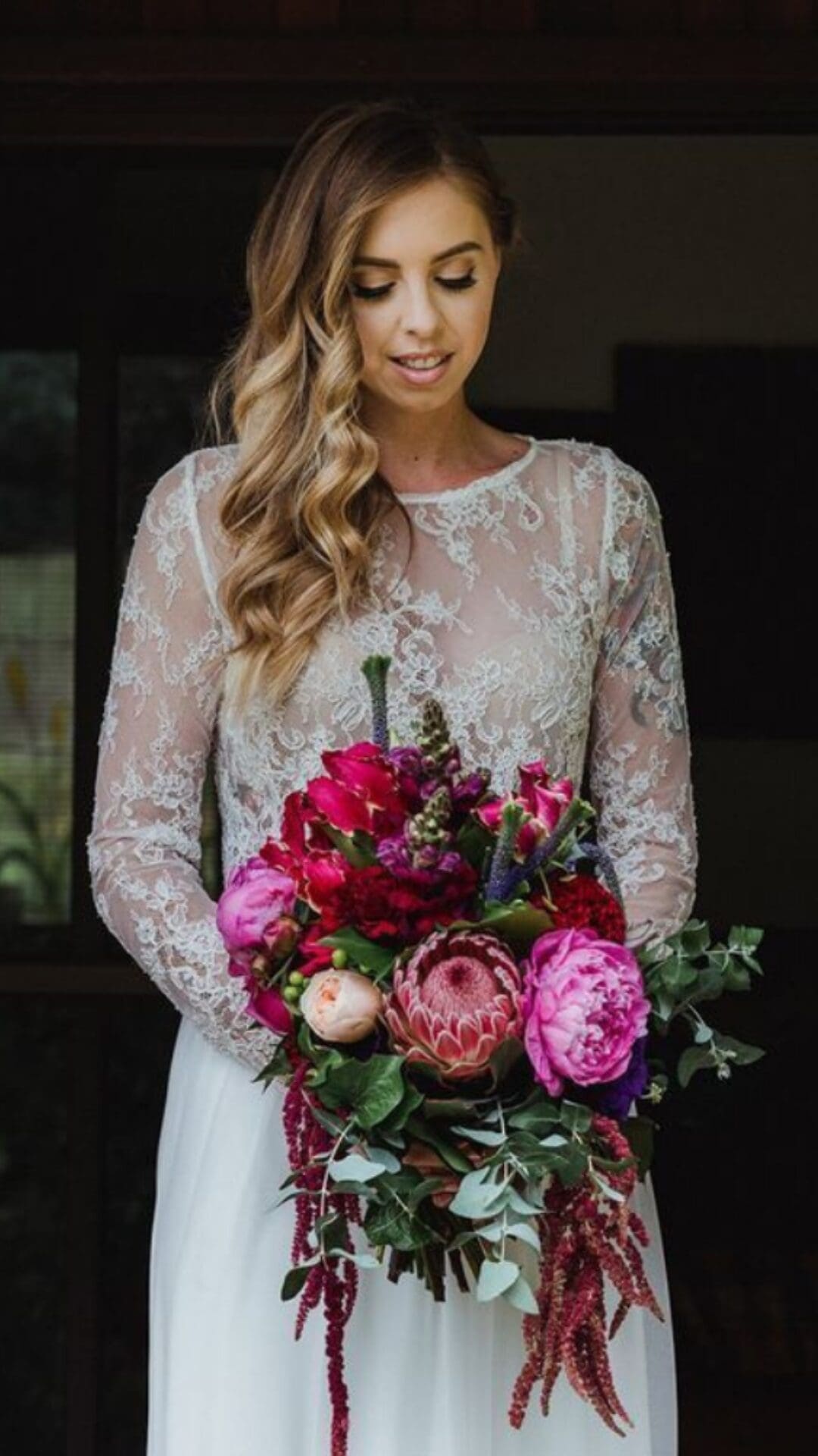 Bride in lace dress holding pink and red wedding flowers