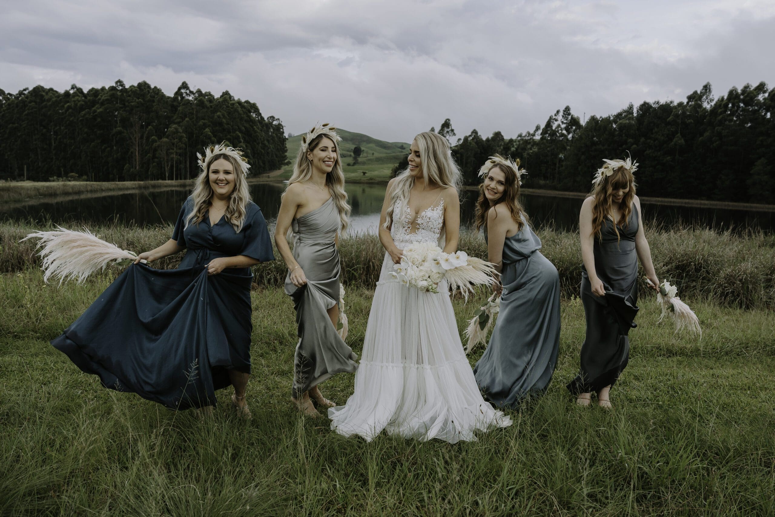 Bridesmaids in mismatched dresses gathered around bride in field