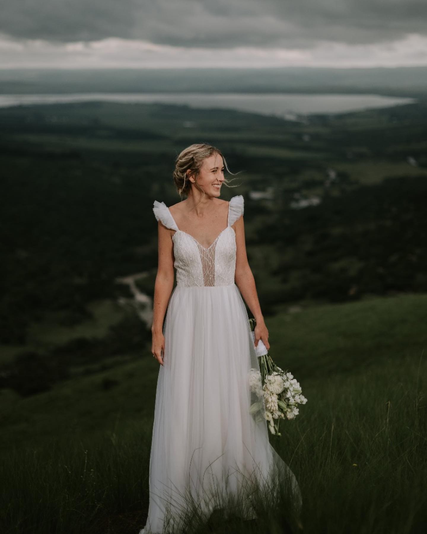 Bride standing in green countryside holding small bouquet