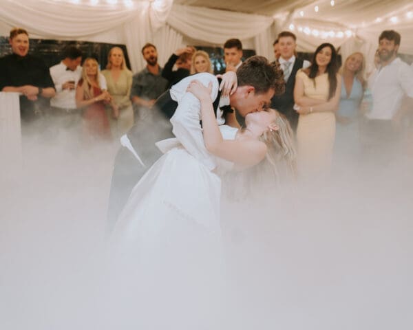 Wedding first dance with groom dipping bride on smoke-filled dancefloor