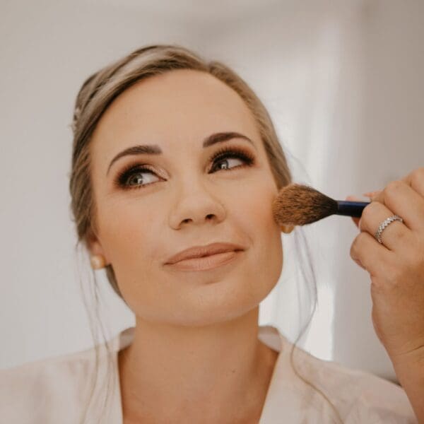 Hand holding blush brush and applying colour to bride's face