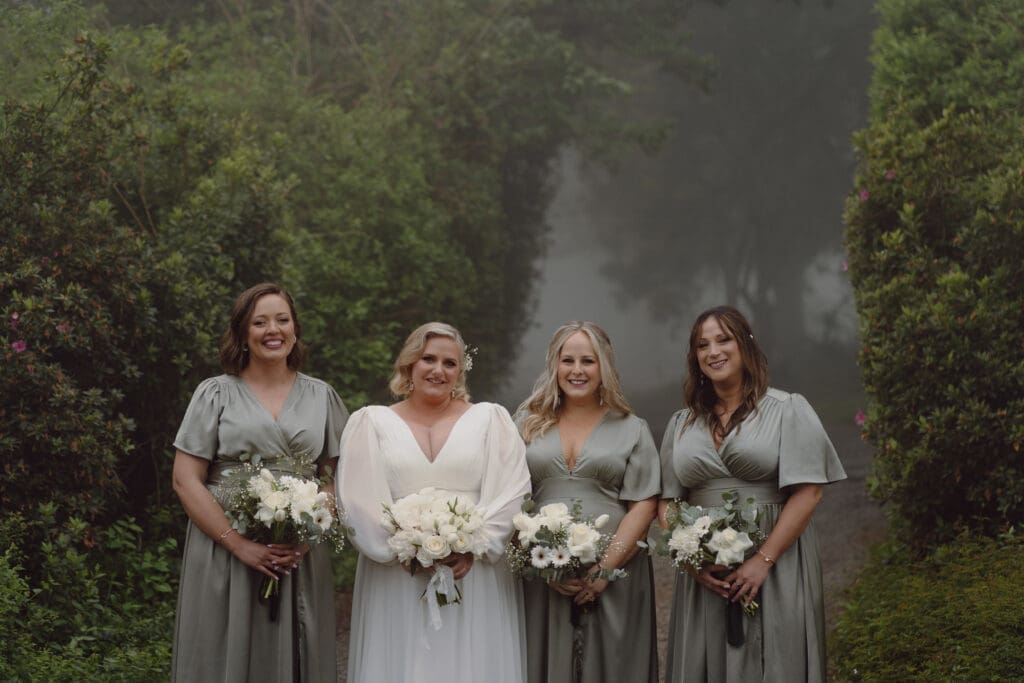 Bride flanked by bridesmaids in sage green with white bouquets