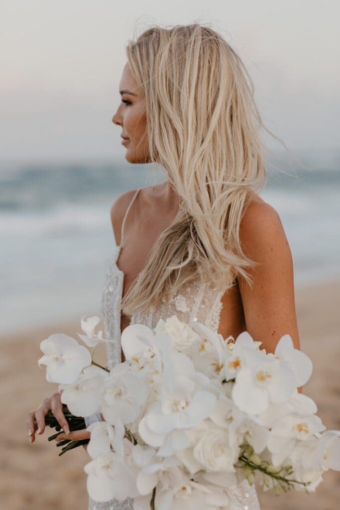 Bride on beach holding all-white bouquet