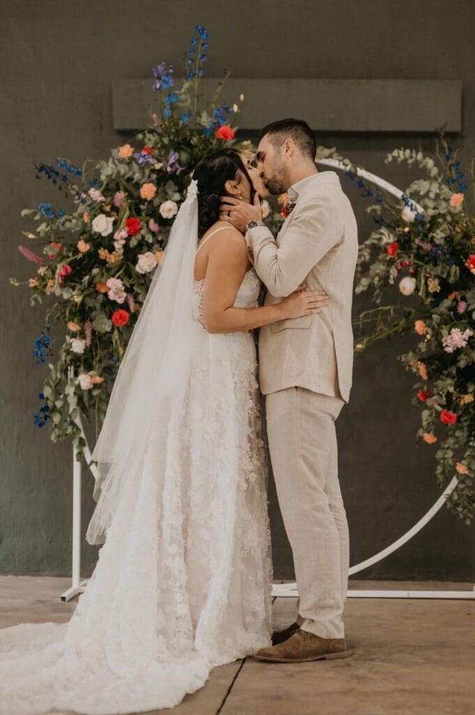 Bride and groom kissing in front of circular floral arch