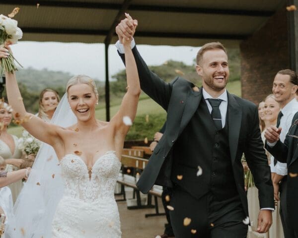 Bride and groom in full cheer as they exit the aisle with hands raised
