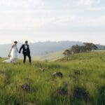 Bride and groom walking hand in hand in lush field at Mission House.
