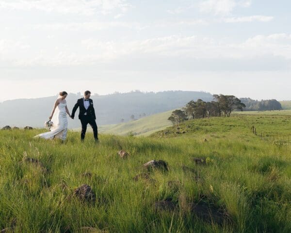 Bride and groom walking hand in hand in lush field at Mission House.