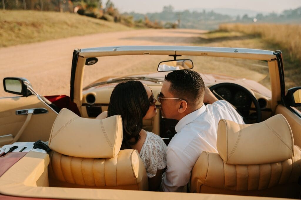 Bride and groom sitting in front seats of vintage car leaning in towards each other