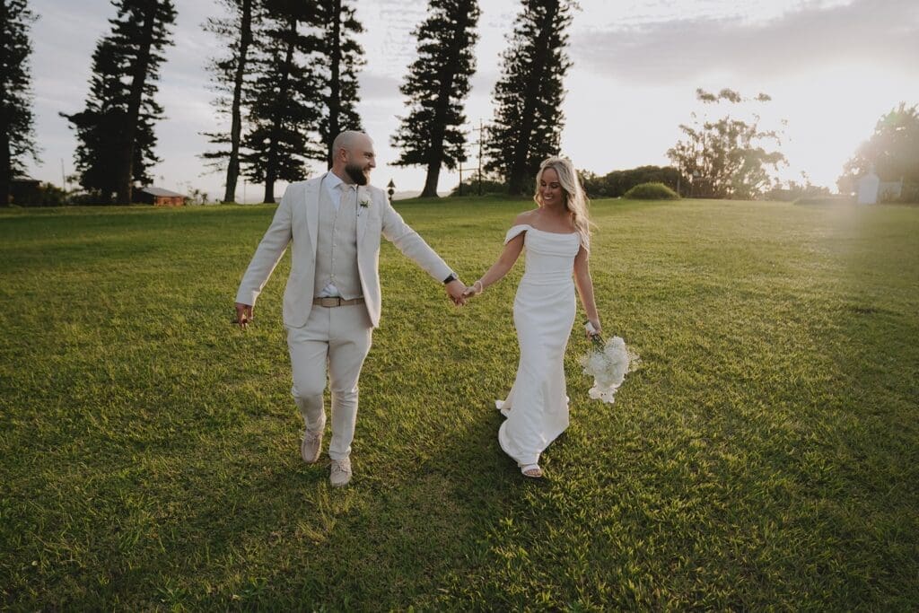 Bride and groom walking hand in hand in grass field.
