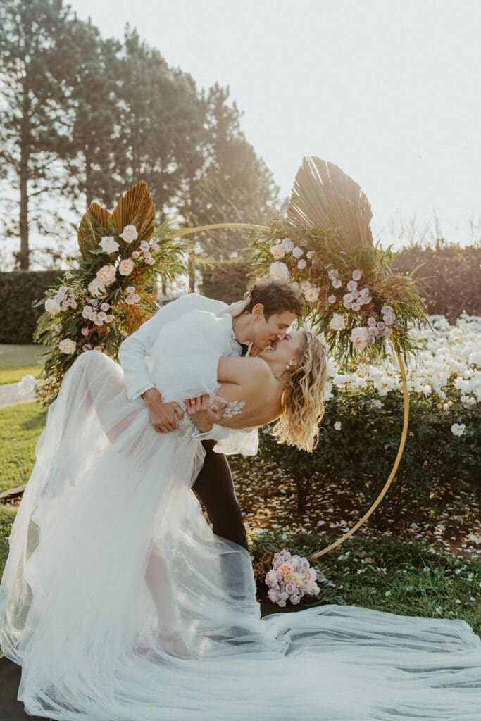 Newly weds doing dip kiss in front of circular floral arch