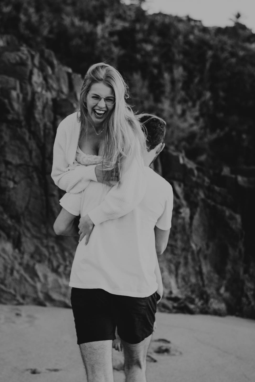 Black and white engagement shoot image of woman hoisted on man's shoulder