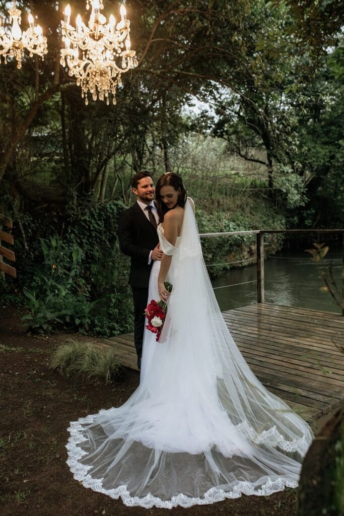 Bride and groom standing together under chandeliers at The River Deck at The Groves