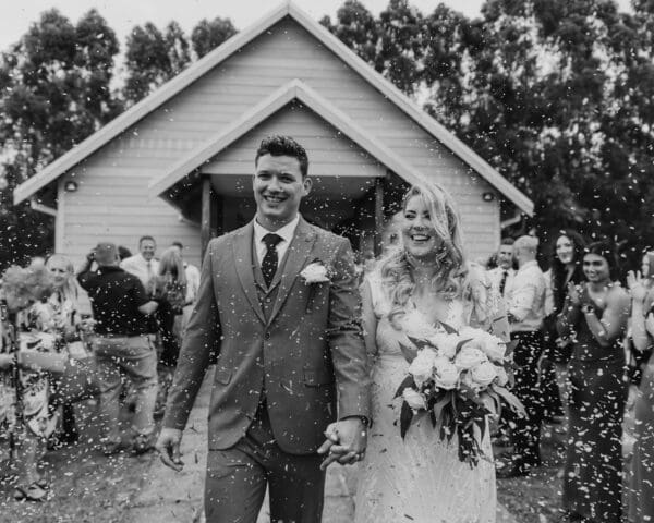 Black and white image of the bride and groom exiting the chapel with confetti toss
