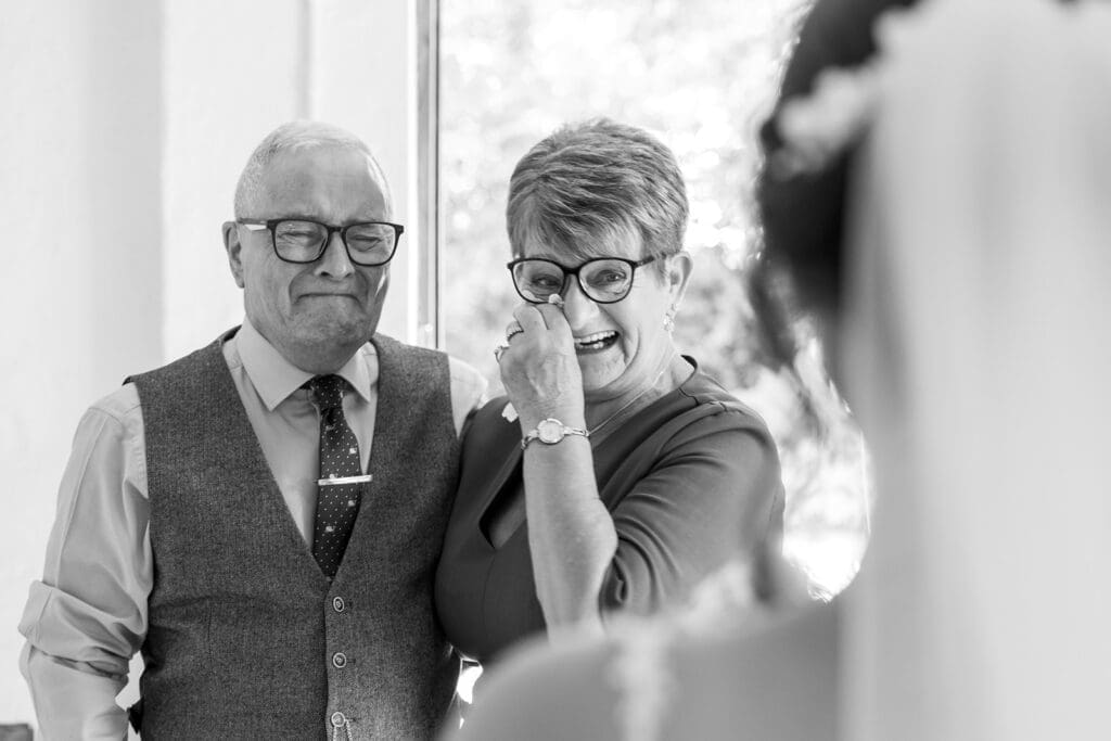 Gray-scale image of tearful first look moment between bride and parents