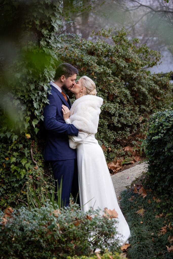 Bride and groom kissing among garden foliage
