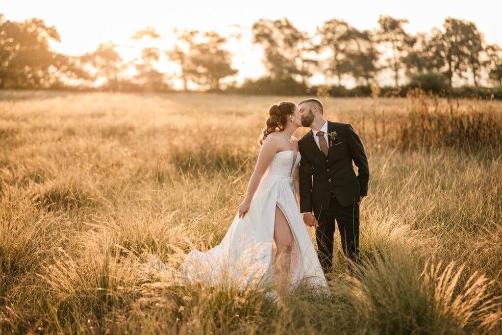 Bride and groom standing in golden grass field leaning in for a kiss