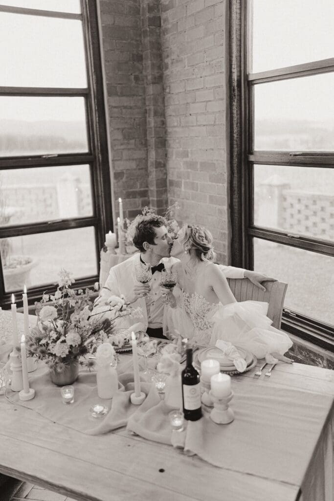 Grayscale image of bride and groom kissing at sweetheart table