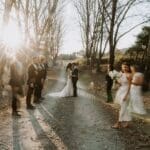 Movement shot of bride and groom standing on dirt road with bridal party running across
