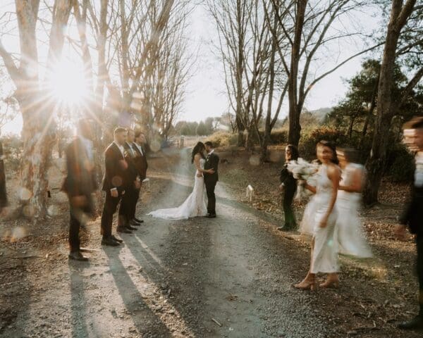 Movement shot of bride and groom standing on dirt road with bridal party running across