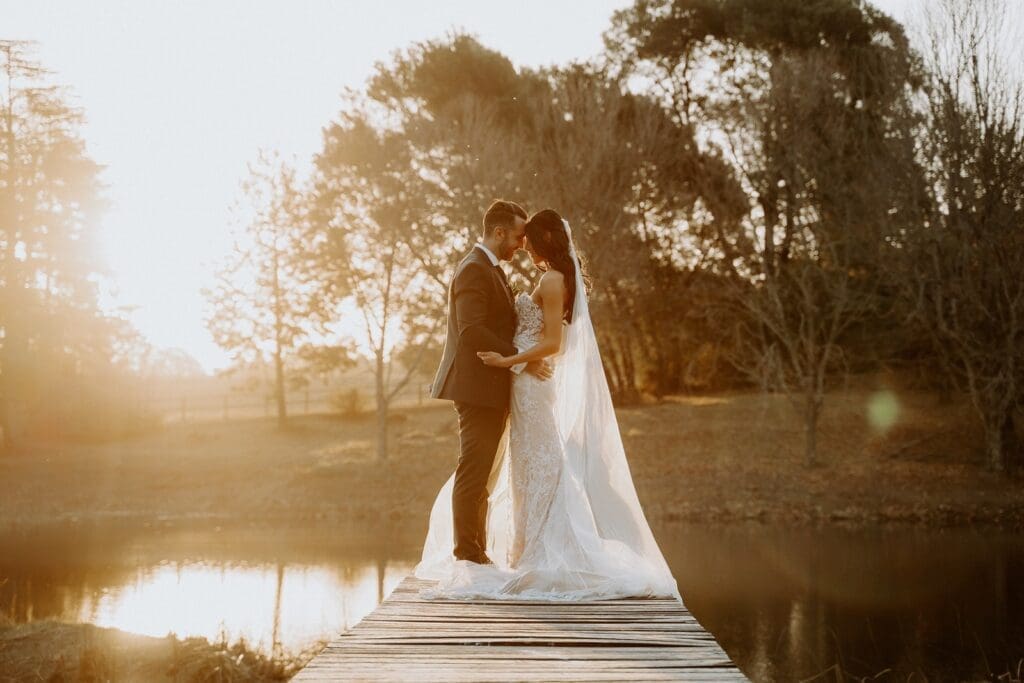 Bride and groom standing facing each other on pier with sunset glow