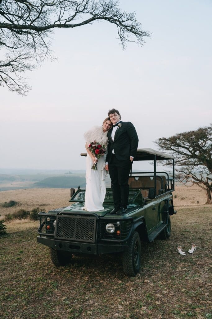 Bride and groom standing on bonnet of game vehicle