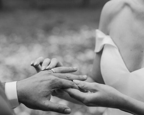 Black and white image of bride placing wedding ring onto grooms finger
