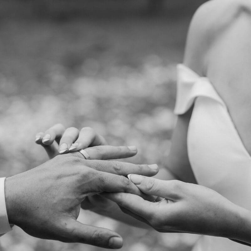 Black and white image of bride placing wedding ring onto grooms finger